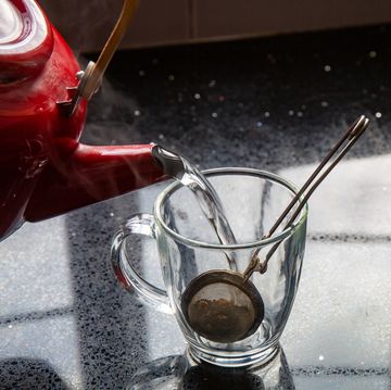pouring boiling water into a glass mug containing a tea infuser