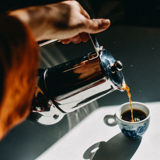 pouring espresso coffee into an espresso cup with a mocha pot