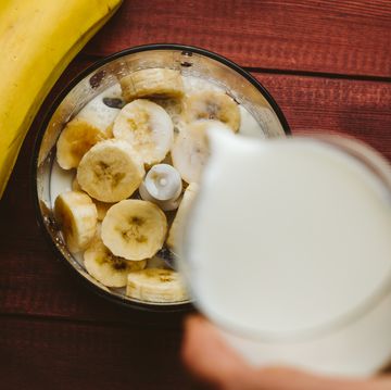 Pouring milk in blender over pieces of bananas, banana smoothie, top view