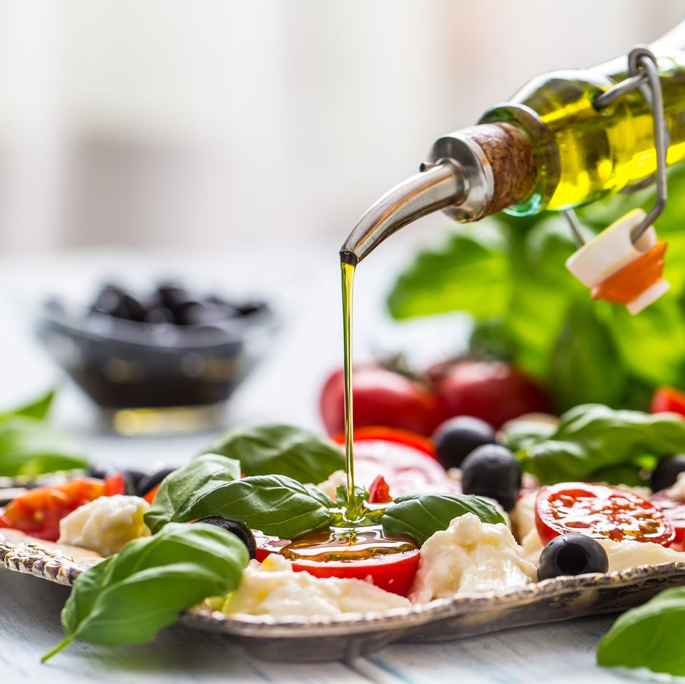 Pouring olive oil on caprese salad. Healthy italian or mediterranean meal