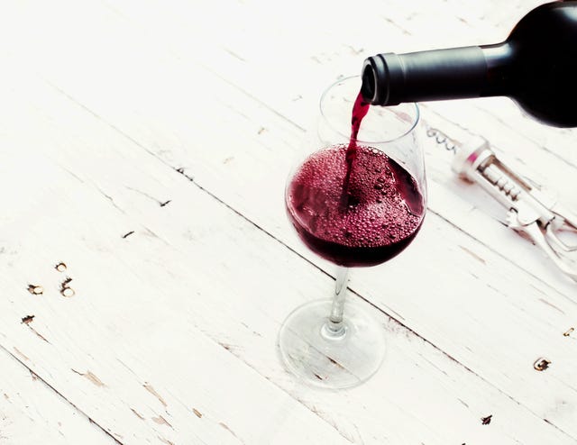 Pouring red  wine from bottle in wine glass on vintage white wooden table  with copyspace.