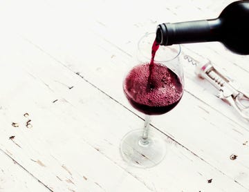 Pouring red  wine from bottle in wine glass on vintage white wooden table  with copyspace.