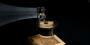 pouring sake into a glass inside a wooden container for drinking or measuring sake