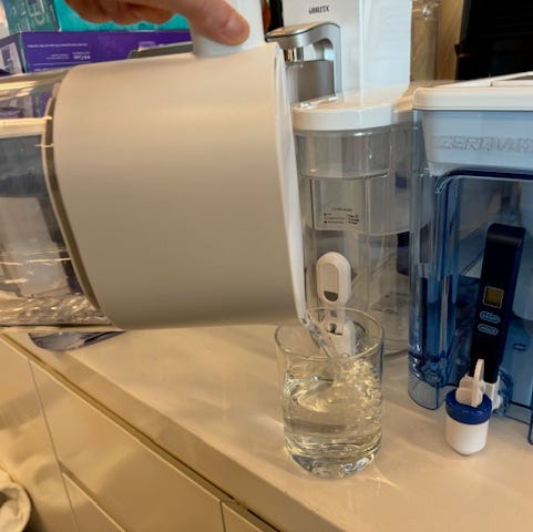 Best water filter pitcher pouring water into a glass on a counter with other water filter pitchers in the background
