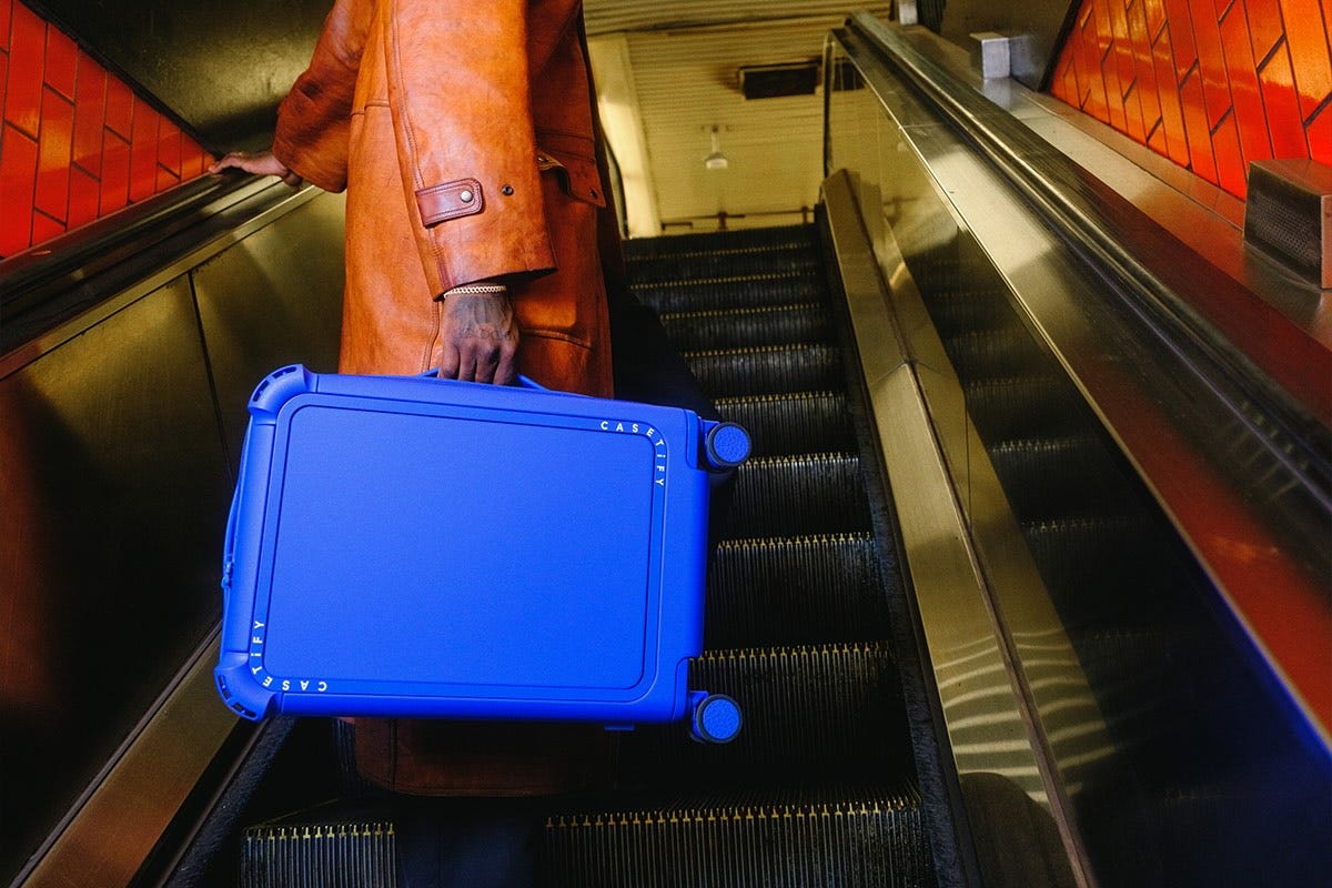 person traversing an escalator while carrying a blue suitcase