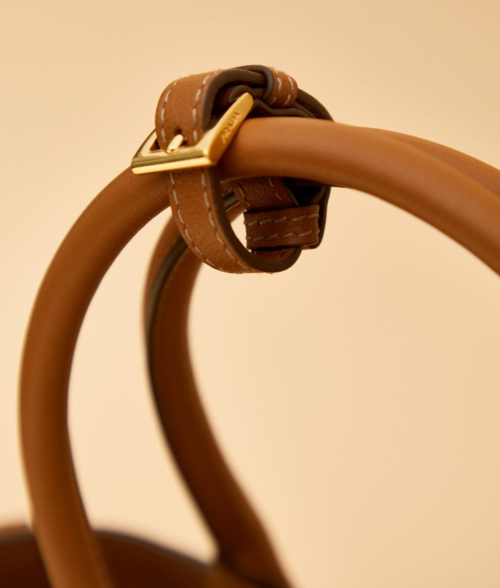 closeup of a brown leather bag handle with a gold buckle