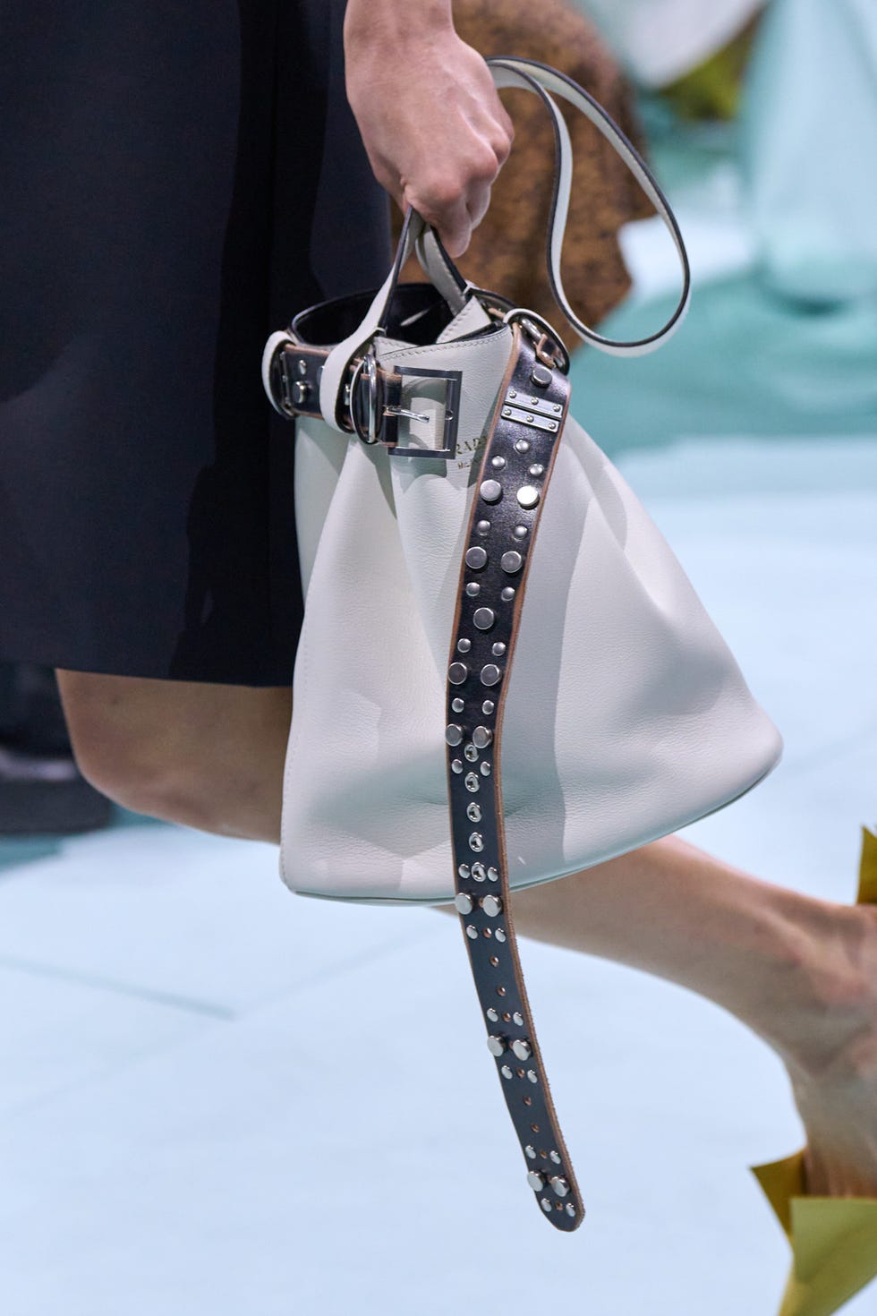 White handbag being held by a person with a unique strap design