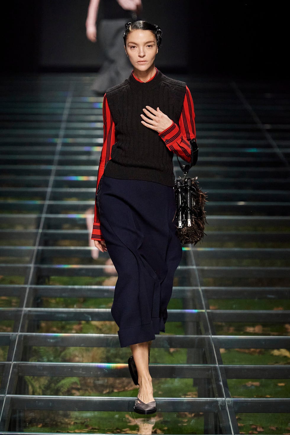 A model walks the runway in a layered outfit with a striped blouse and a knitted vest.