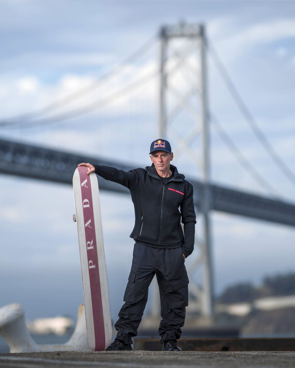 a person posing with a branded surfboard near a large bridge