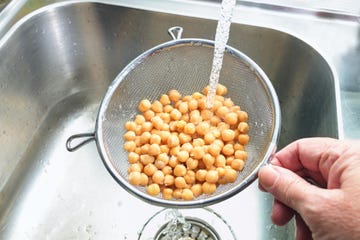 pre cooked canned chickpeas are rinsed with water in a sieve over the sink before being used in various dishes, healthy legumes are rich in protein, fiber and minerals, copy space