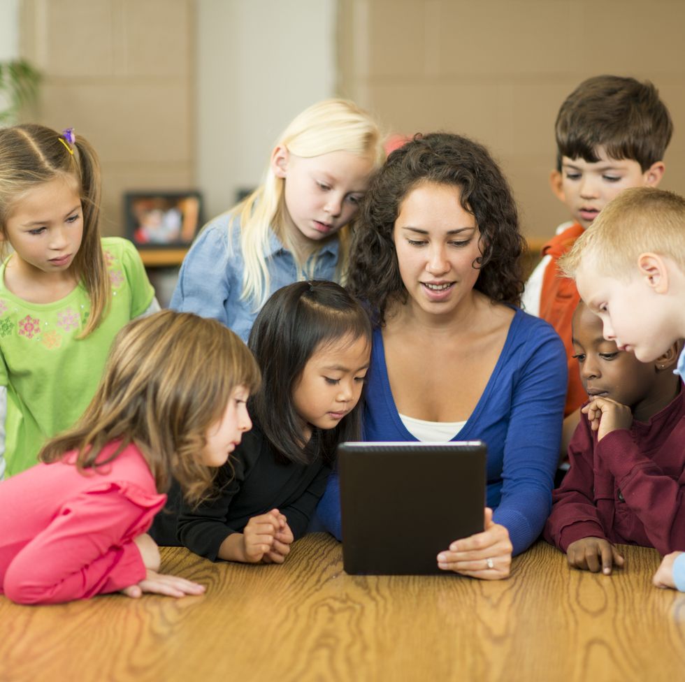 jobs for stay at home moms - Pre-schoolers in classroom gathered around a woman with a tablet