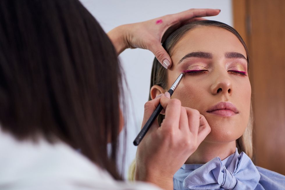 precise makeup artist using a thin eye liner brush to apply a purple eyeliner for complete make up look