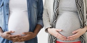 two pregnant women standing next to each other holding bellies