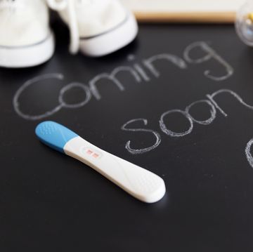 coming soon words on black chalkboard with a heart and positive pregnancy test, white baby shoes and rattle