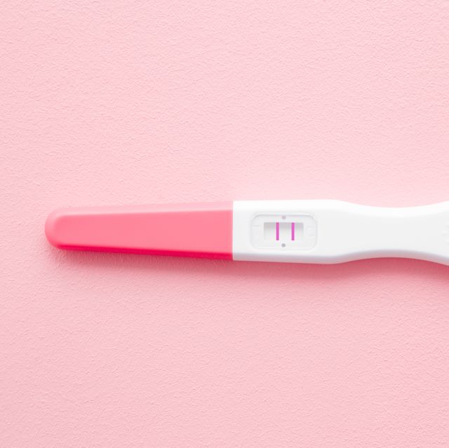 pregnancy test with two stripes on pastel pink background positive result closeup top down view