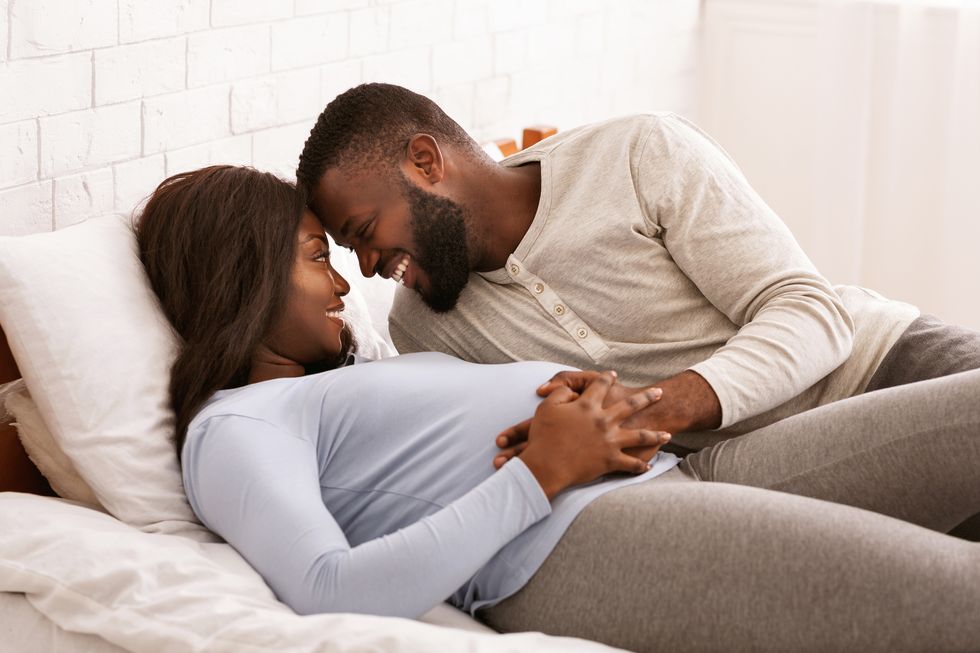 pregnant couple in love cuddling in bed at home