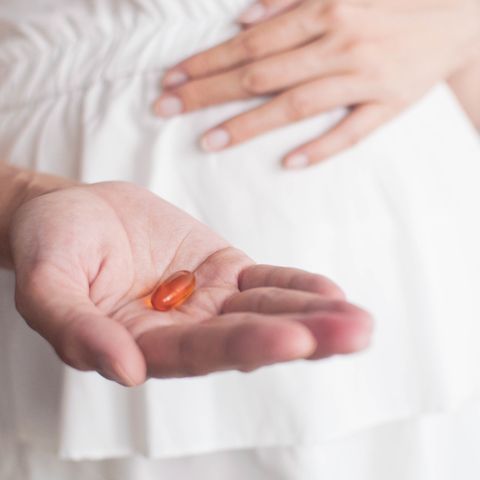 a pregnant southeast asian woman is holding a medicine gel capsule