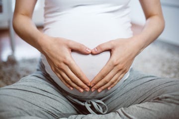 unrecognizable female sitting on the carpet in domestic room and making heart symbol on her belly