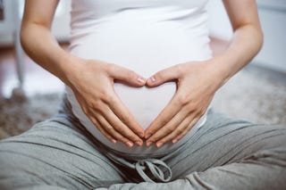 unrecognizable female sitting on the carpet in domestic room and making heart symbol on her belly