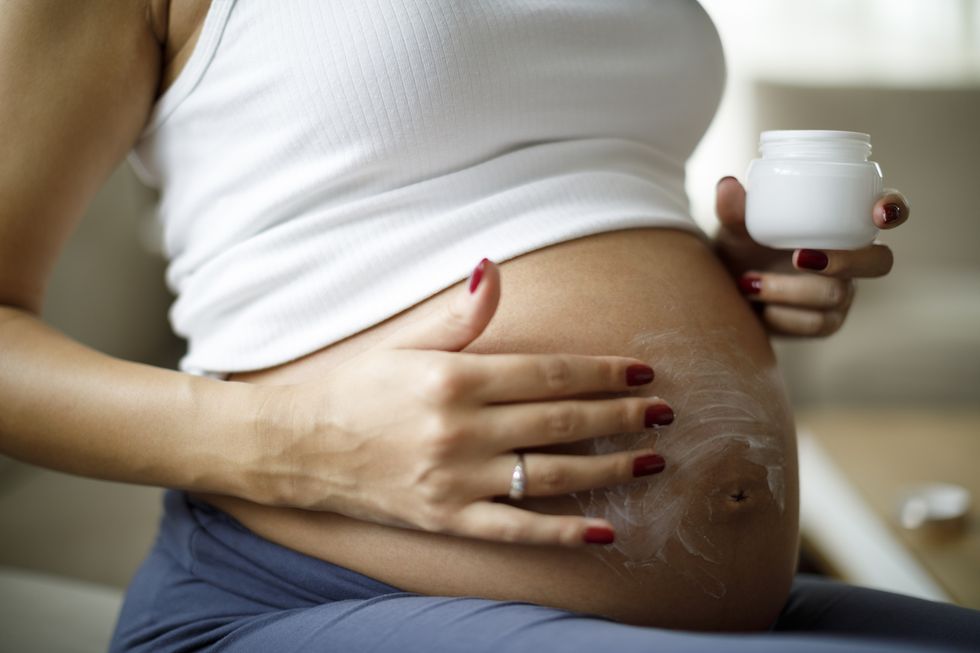 pregnant woman applying skincare cream on her belly to prevent stretch mark