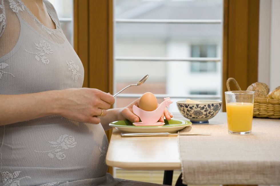 pregnant woman cracking a boiled egg at breakfast
