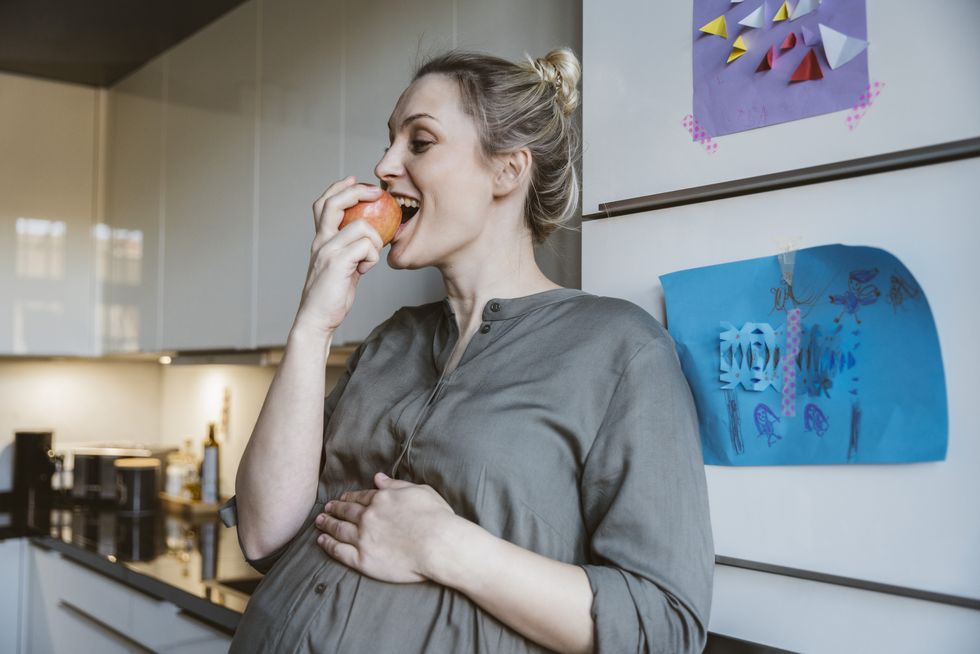 pregnant woman eating an apple in kitchen at home