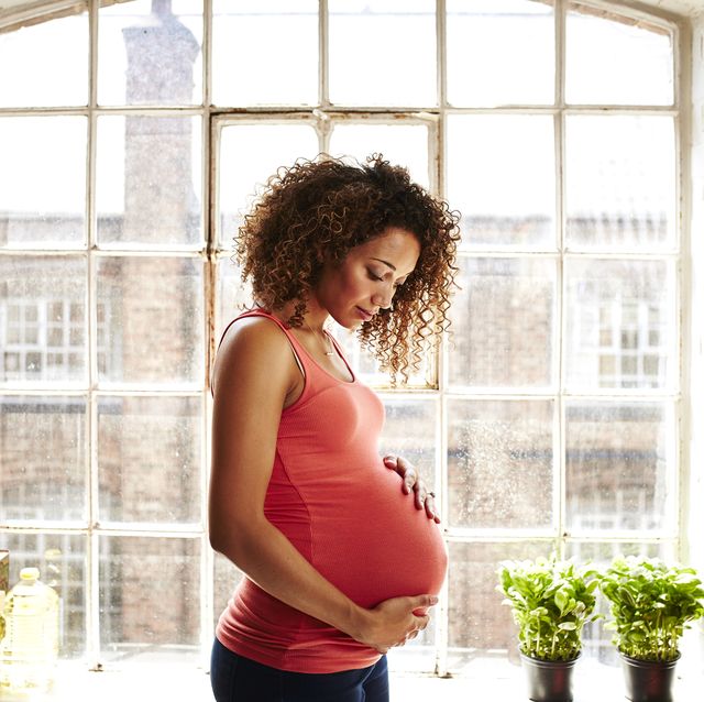 a pregnant woman holds her bump in kitchen window