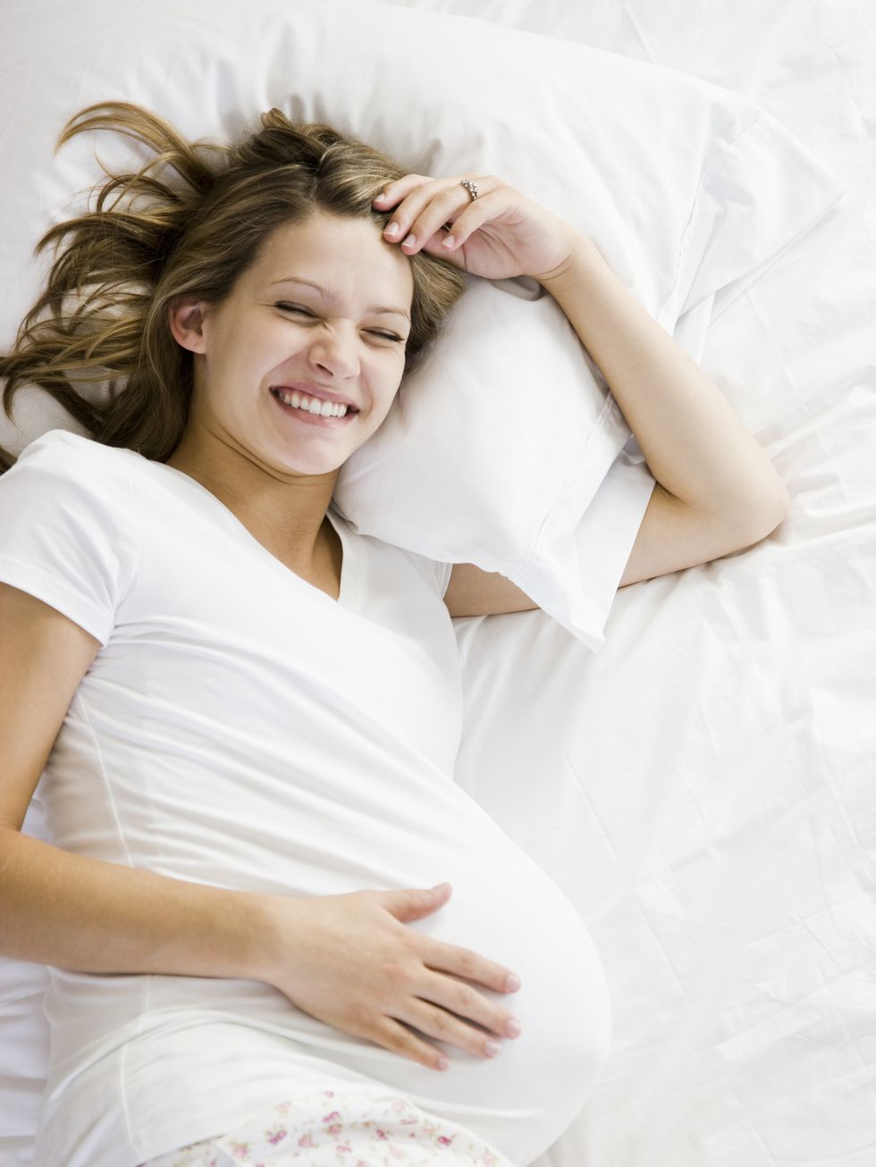 mujer embarazada tumbada en la cama riéndose