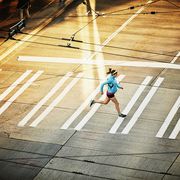 pregnant woman running across sidewalk during early morning run on empty city street