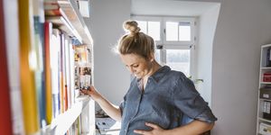 pregnant woman standing at bookshelf at home