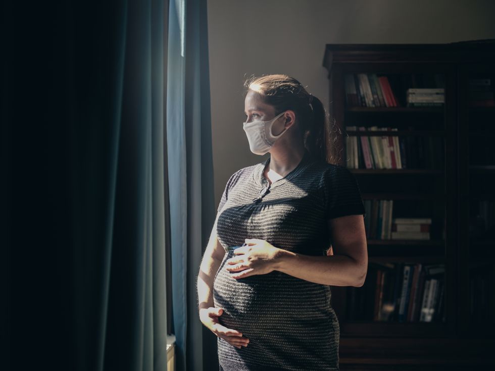 pregnant woman with face mask standing in front of window