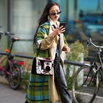 a woman wearing sunglasses and a green and beige coat holding a phone
