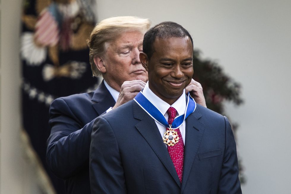 donald trump placing a medal around the neck of tiger woods as he stands behind him