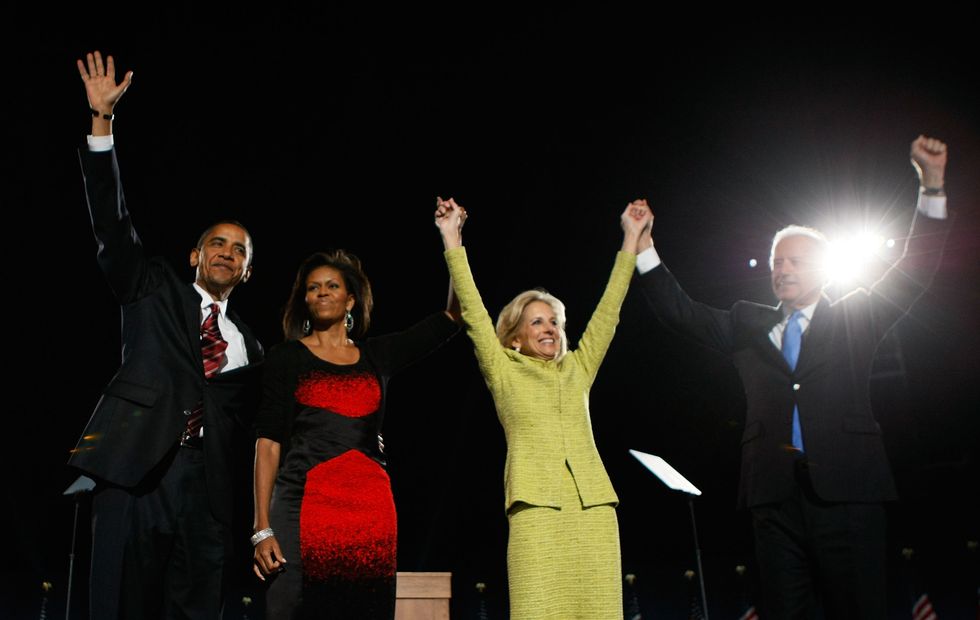 barack and michelle obama wave to supporters on a stage, standing next to joe and jill biden raising their hands in the air