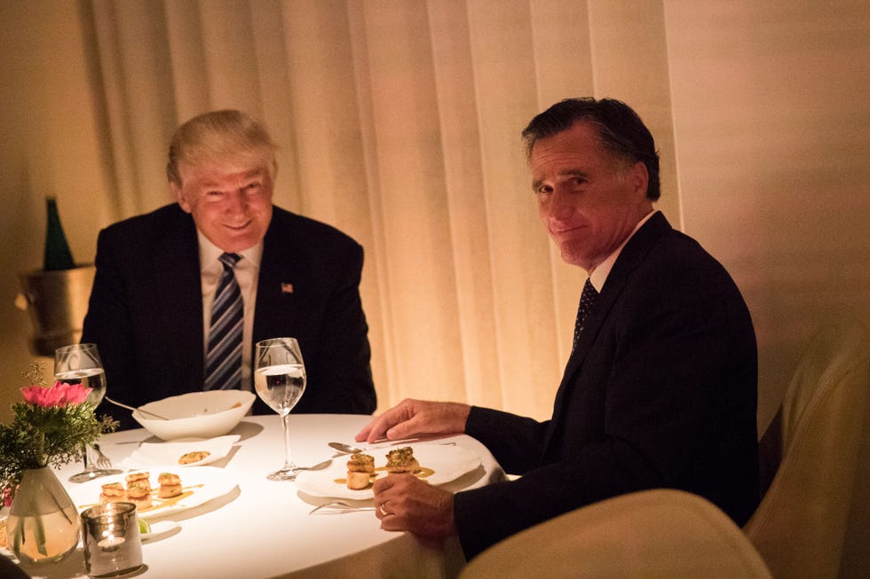 donald trump and mitt romney sitting together at a restaurant table, looking directly into the camera, with trump smiling and romney grimacing slightly