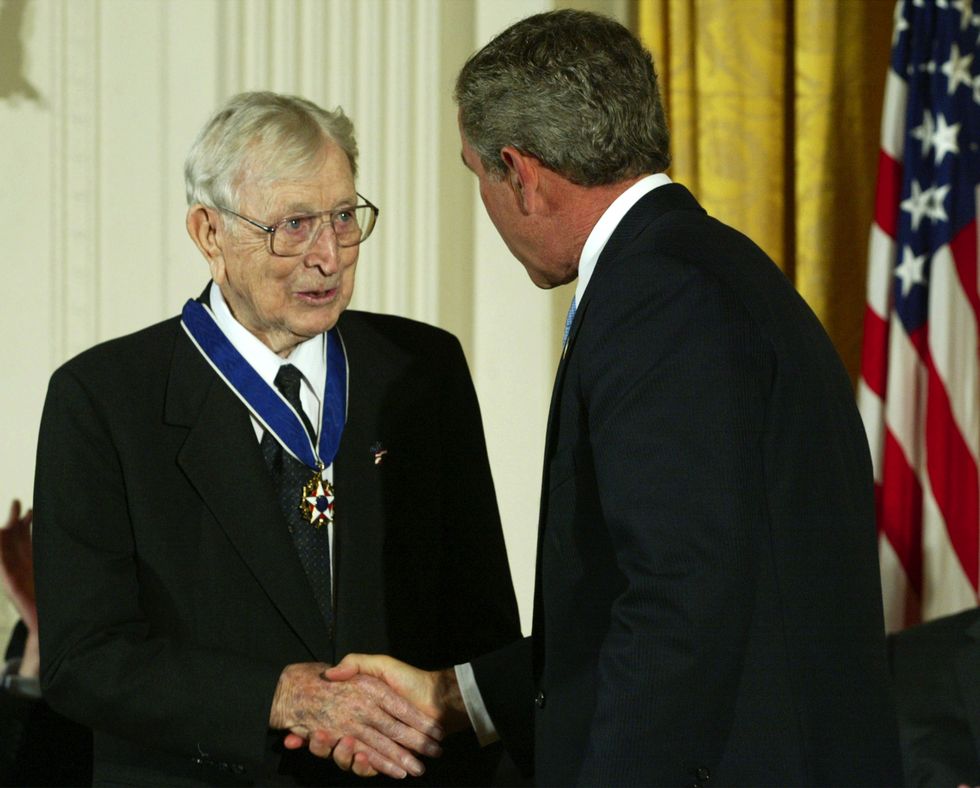 john wooden, wearing a black suit and the presidential medal of freedom around his neck, shakes hands with george w bush, who is also wearing a black suit