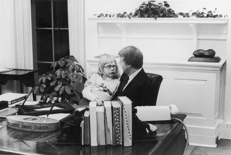 jimmy carter talks with his daughter amy who sits in his lap in the oval office in 1978
