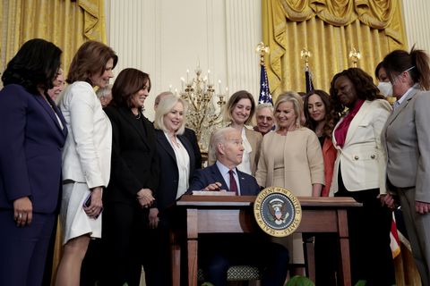 president biden signing the bill into law surrounded by a group of women including cheri bustos, kamala harris, and kirsten gillibrand