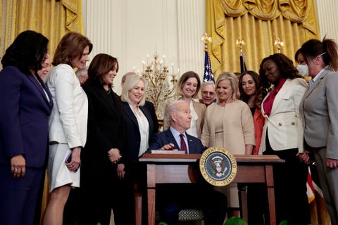 president biden signing the bill into law surrounded by a group of women including cheri bustos, kamala harris, and kirsten gillibrand