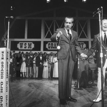 richard nixon and roy acuff hold hands while standing on a stage, nixon plays with a yo yo as a crowd of people watches from the background