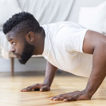 young black man exercising in his house gym, doing push ups, side view, free space