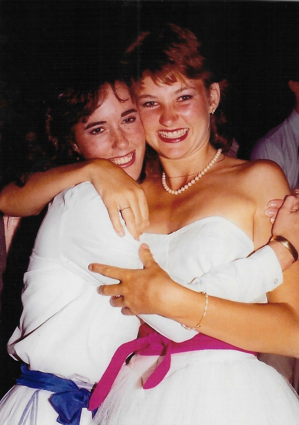 two women in white dresses hug