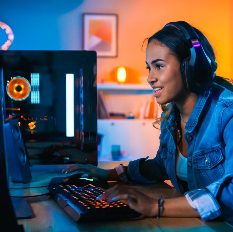 pretty and excited black gamer girl in headphones is playing first person shooter online video game on her computer room and pc have colorful neon led lights