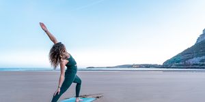 pretty blonde woman doing yoga in front of the sea on the beach meditating on blue mat at sunrise