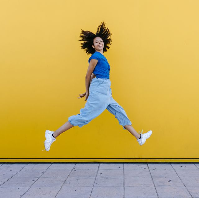 pretty woman jumping for joy in front of yellow wall