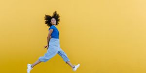 pretty woman jumping for joy in front of yellow wall