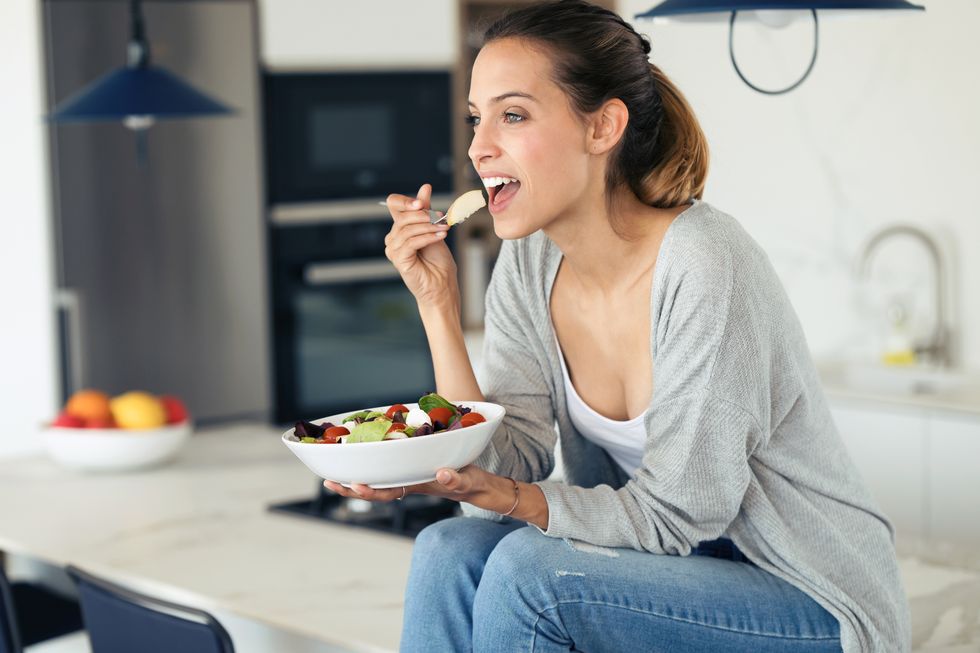 pretty young woman eating salad while sitting in the kitchen at home