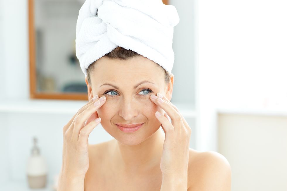 pretty young woman with a towel putting cream on her face in the bathroom