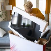 after online shopping at home during lockdown a woman takes delivery of her new smart tv, lifting it carefully from its protective wrapping inside her modern home