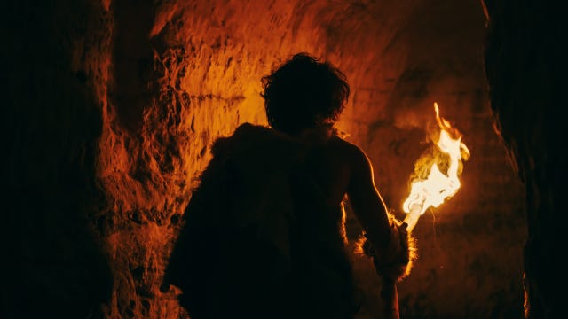 primeval caveman wearing animal skin exploring cave at night holding torch with fire looking at drawings on the walls at night neanderthal searching safe place to spend the night back view